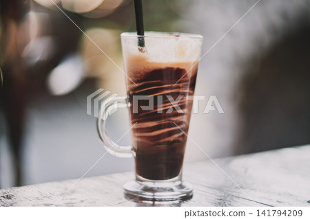 Close-up of a refreshing iced coffee beverage served in a clear glass mug on a wooden table Close-up of a refreshing iced coffee beverage served in a clear glass mug on a wooden table 141794209