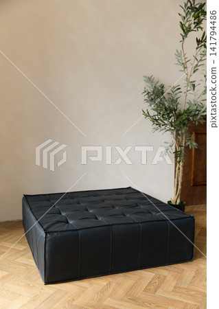 Modern black tufted leather square ottoman in minimalist bright interior with sunlight Modern black tufted leather square ottoman in minimalist bright interior with sunlight 141794486