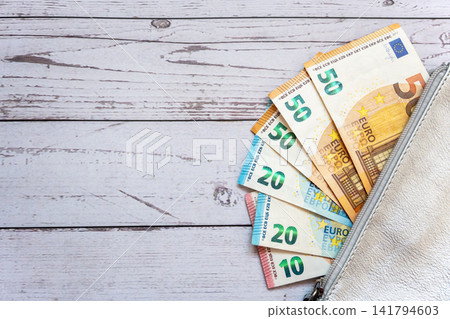 Leader silver partmone with cash euro money. Paper bills in the wallet for commerce concept. White wood table background. Leader silver partmone with cash euro money. Paper bills in the wallet for commerce concept. White wood table background. 141794603