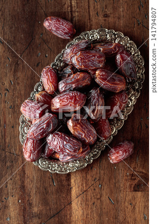 Dried dates fruit in silver tray on a wooden table. Dried dates fruit in silver tray on a wooden table. 141794807