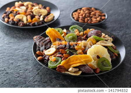 Dried tropical fruits, nuts, and raisins in black plate. Dried tropical fruits, nuts, and raisins in black plate. 141794832