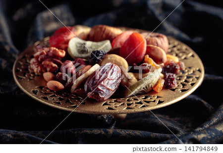 Dried tropical fruits and nuts in a golden bowl. 141794849