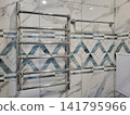 In the bathroom, a metal towel warmer hangs on the wall made of gray tiles. 141795966