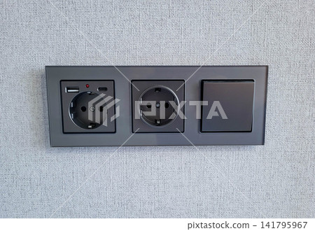 A gray block with a switch and sockets on a light colored wall. A gray block with a switch and sockets on a light colored wall. 141795967