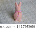A pink rabbit toy with a bow is standing on a beige blanket. Easter concept. 141795969