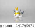 An egg with yellow rabbit ears sits in a white egg shell with blue forget-me-nots 141795971