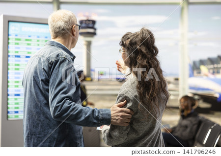 Joyful couple, checking flight status, and boarding gate information, elderly man and woman standing near airport screen in terminal concourse. Senior couple using screen for wayfinding. Joyful couple, checking flight status, and boarding gate information, elderly man and woman standing near airport screen in terminal concourse. Senior couple using screen for wayfinding. 141796246