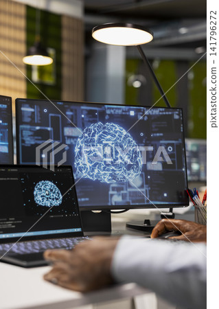 Close up of engineer in office relying on AI tech to run tasks across multiple devices, monitoring progress on screens. IT expert uses neural networks to develop artificial intelligence models Close up of engineer in office relying on AI tech to run tasks across multiple devices, monitoring progress on screens. IT expert uses neural networks to develop artificial intelligence models 141796272