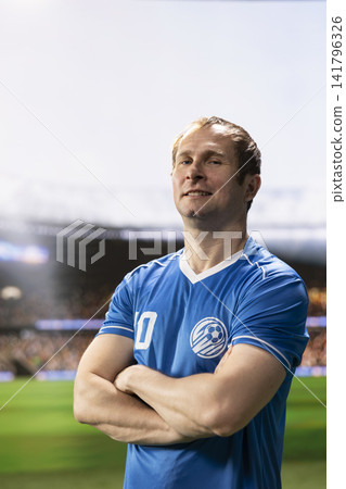 Portrait of football player standing with arms crossed in blue jersey on pitch, entering stadium before soccer game. Footballer ready to play match with blurred background. Portrait of football player standing with arms crossed in blue jersey on pitch, entering stadium before soccer game. Footballer ready to play match with blurred background. 141796326