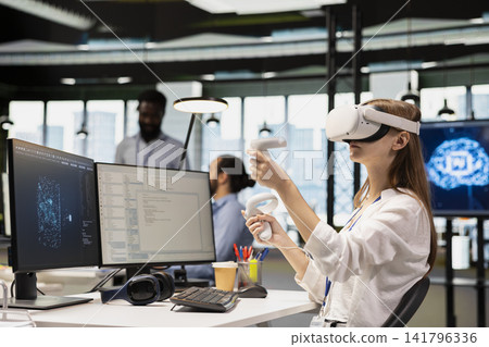 Junior programmer using virtual reality at work, testing generative AI machine learning algorithms. Young worker wearing VR goggles equipment scaling productivity with AI large language model code Junior programmer using virtual reality at work, testing generative AI machine learning algorithms. Young worker wearing VR goggles equipment scaling productivity with AI large language model code 141796336