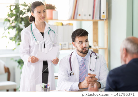 Senior man client of medical clinic sits opposite male and female doctor and communicates with specialists Senior man client of medical clinic sits opposite male and female doctor and communicates with specialists 141796371