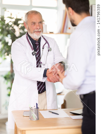 Elderly male doctor shaking hands with adult male patient Elderly male doctor shaking hands with adult male patient 141796389