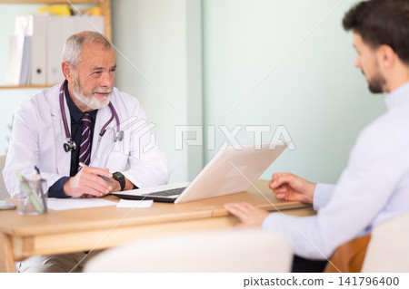 Man client of medical clinic sits opposite mature male doctor and communicates with specialist Man client of medical clinic sits opposite mature male doctor and communicates with specialist 141796400