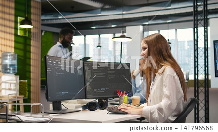 Young female programmer using computer to write code, developing machine learning APIs. Junior developer troubleshooting software errors and faults using artificial intelligence, camera A Young female programmer using computer to write code, developing machine learning APIs. Junior developer troubleshooting software errors and faults using artificial intelligence, camera A 141796568