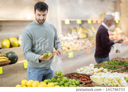 Man stands in the middle of a supermarket near a citrus fruit counter Man stands in the middle of a supermarket near a citrus fruit counter 141796733