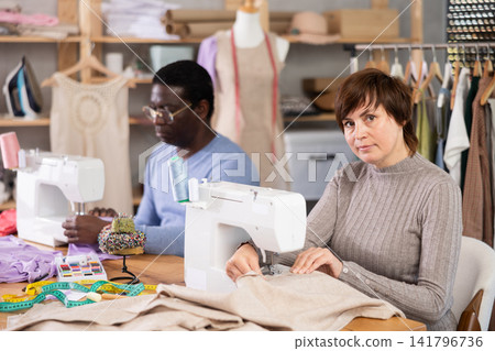 Woman tailor and African male companion sew clothes in sewing machine Woman tailor and African male companion sew clothes in sewing machine 141796736
