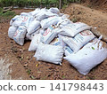 Stacked white sacks of animal feed for farm livestock in a rustic outdoor rural setting on dirt ground 141798443