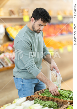 man standing in supermarket near counter and putting green beans in bag man standing in supermarket near counter and putting green beans in bag 141798487