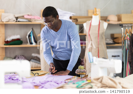 African man seamstress cuts fabric on cutting table African man seamstress cuts fabric on cutting table 141798519