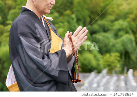 墓地裡,一位僧侶雙手合十祈禱,手中拿著念珠。 墓地裡,一位僧侶雙手合十祈禱,手中拿著念珠。 141798634