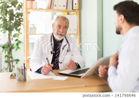 Elderly male doctor talking with adult male patient in medical office Elderly male doctor talking with adult male patient in medical office 141798646
