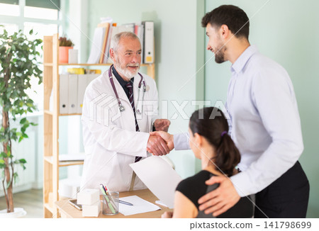Medical appointment, senior male doctor and husband patient shake hands, family medical appointment Medical appointment, senior male doctor and husband patient shake hands, family medical appointment 141798699