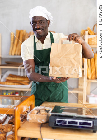 Male baker holding a brown paper bag in a bakery Male baker holding a brown paper bag in a bakery 141798908