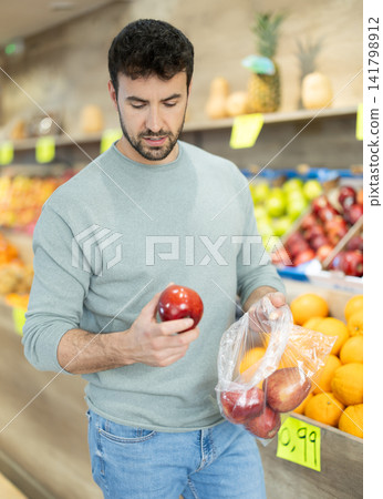 Man stands in a farm shop and chooses delicious ripe apples Man stands in a farm shop and chooses delicious ripe apples 141798912