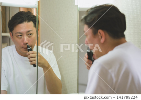 一位四十多歲的男子在浴室鏡子前修剪鼻毛。 一位四十多歲的男子在浴室鏡子前修剪鼻毛。 141799224