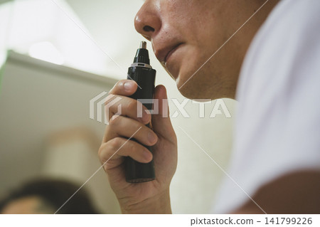 特寫鏡頭:一隻手正在用鼻毛修剪器修剪鼻子。 特寫鏡頭:一隻手正在用鼻毛修剪器修剪鼻子。 141799226