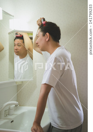 一位 40 歲男子的護髮流程:他走到水槽邊,用電動頭皮梳刺激頭皮。 一位 40 歲男子的護髮流程:他走到水槽邊,用電動頭皮梳刺激頭皮。 141799283