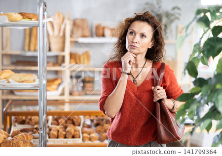 Woman in casual clothes chooses hot croissants for breakfast in bakery 141799364