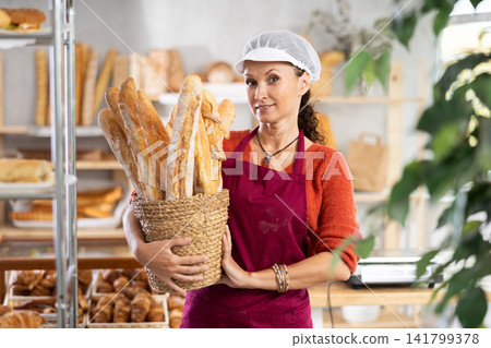 Female bakery employee offering bread and different baguettes for sale Female bakery employee offering bread and different baguettes for sale 141799378