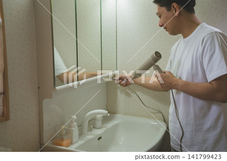A 40-year-old man plugs his hairdryer into the outlet above the sink as part of his hair care routine. A 40-year-old man plugs his hairdryer into the outlet above the sink as part of his hair care routine. 141799423