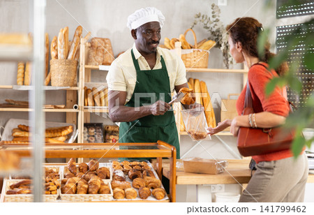 Baker places fresh croissants in plastic bag for female customer Baker places fresh croissants in plastic bag for female customer 141799462