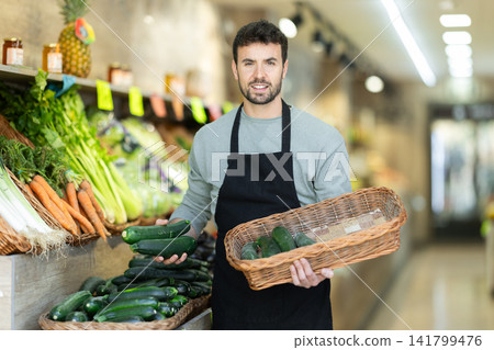 Owner of a farm store holds a zucchini in his hands Owner of a farm store holds a zucchini in his hands 141799476
