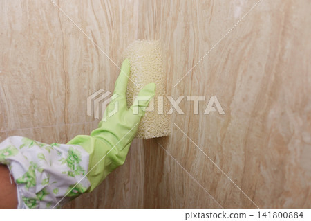 Cleaning a wall in the bathroom with a sponge and gloves Cleaning a wall in the bathroom with a sponge and gloves 141800884