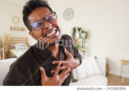 Man clutches chest in living room, clearly in pain Man clutches chest in living room, clearly in pain 141800894