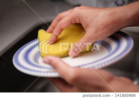 Washing a plate with a sponge in a kitchen sink Washing a plate with a sponge in a kitchen sink 141800906