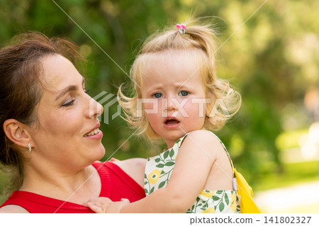 Smiling Mother Holding Curious Toddler Daughter in Park Smiling Mother Holding Curious Toddler Daughter in Park 141802327