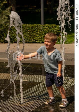 Young Boy Reaching Toward Outdoor Fountain Water Jet Young Boy Reaching Toward Outdoor Fountain Water Jet 141802502