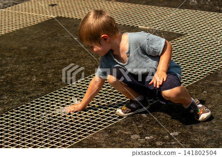 Young Boy Crouching to Touch Ground Fountain Jet Young Boy Crouching to Touch Ground Fountain Jet 141802504