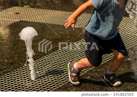 Young Boy Running Beside Small Ground Fountain Jet Young Boy Running Beside Small Ground Fountain Jet 141802505