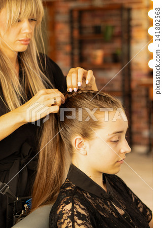 Hairstylist Wrapping Braid Around Teen Client Ponytail In Salon Hairstylist Wrapping Braid Around Teen Client Ponytail In Salon 141802568