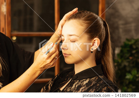 Makeup Artist Applying Eyeshadow To Teen Client In Salon Makeup Artist Applying Eyeshadow To Teen Client In Salon 141802569