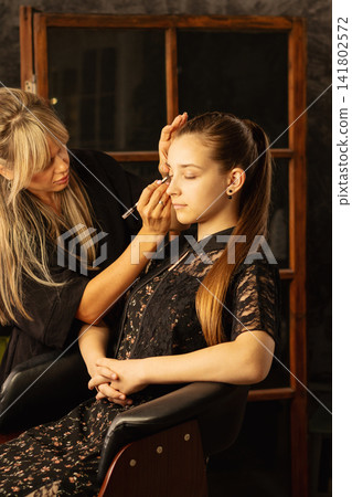 Makeup Artist Applying Eye Pencil To Teen Client In Salon Makeup Artist Applying Eye Pencil To Teen Client In Salon 141802572