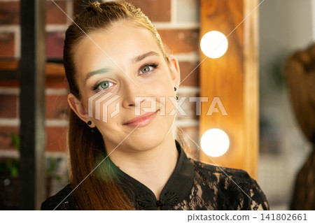 Teen Girl Smiling Near Illuminated Mirror In Beauty Salon Teen Girl Smiling Near Illuminated Mirror In Beauty Salon 141802661