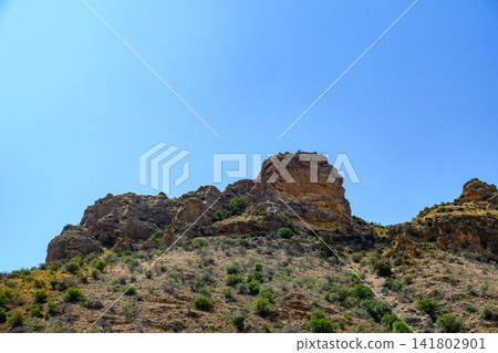 Rocky terrain with sparse vegetation under bright blue sky Rocky terrain with sparse vegetation under bright blue sky 141802901