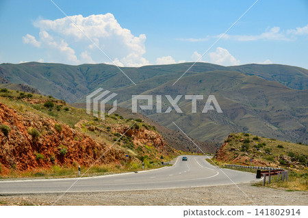 Mountain road with car, rocky hillsides, blue sky with clouds Mountain road with car, rocky hillsides, blue sky with clouds 141802914