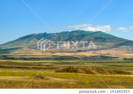 Breathtaking mountain vista framed by golden plains and cloudless blue sky 141802953